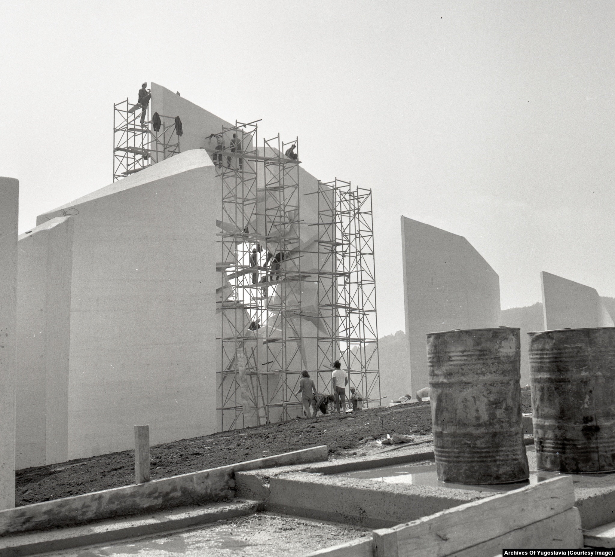 The Kadinjača monument’s tall central void wrapped in metal scaffolding against a pale sky.