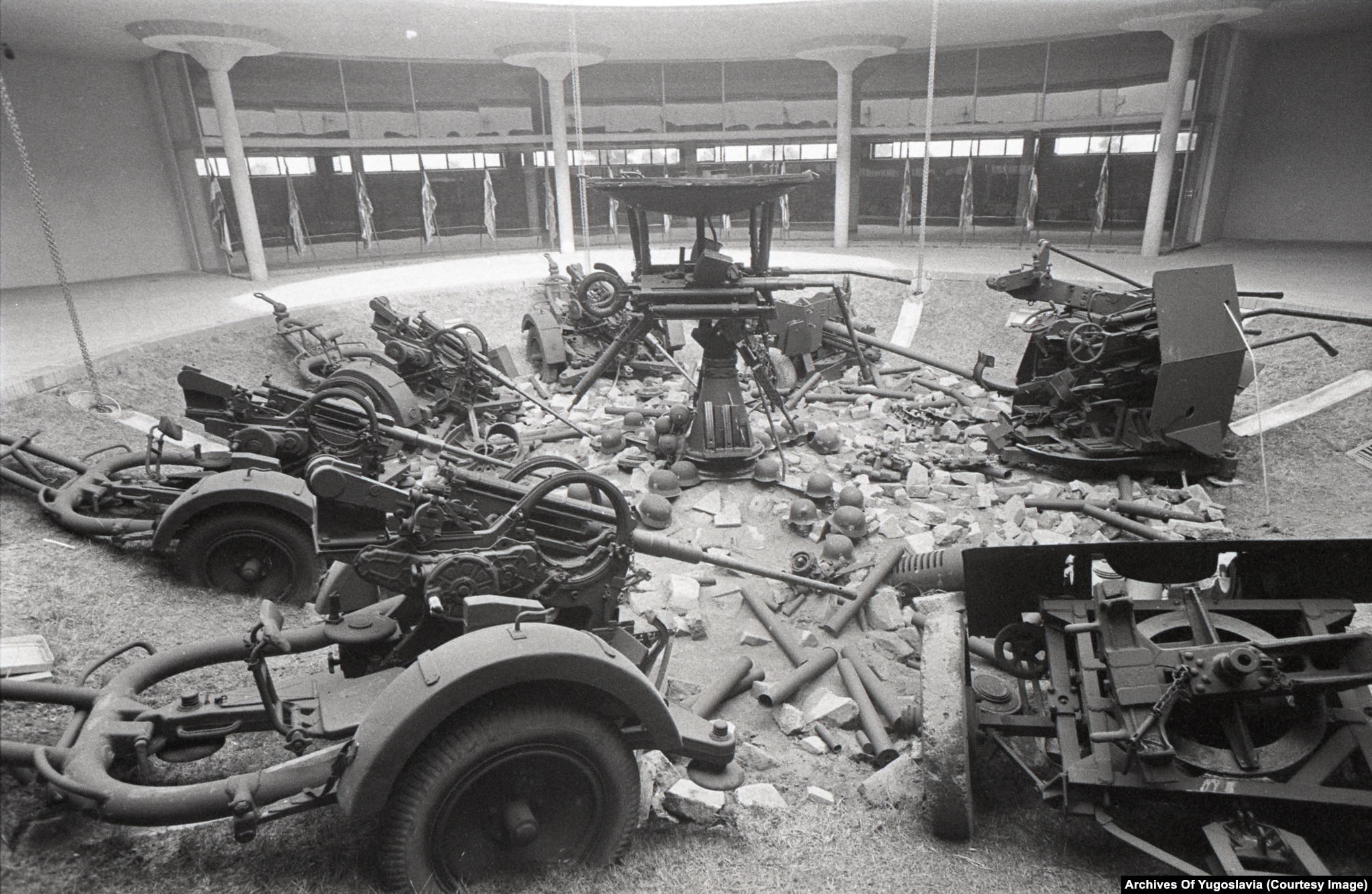 Several wheeled artillery guns arranged on display inside the circular interior of the Sremski Front memorial.