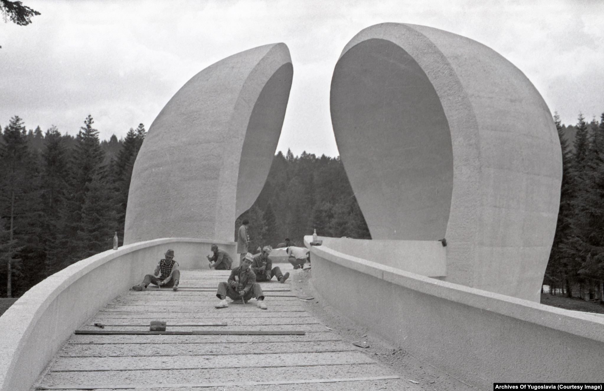 Construction workers with tools on a paved approach path at the Grmeč hospital monument site, 1979.