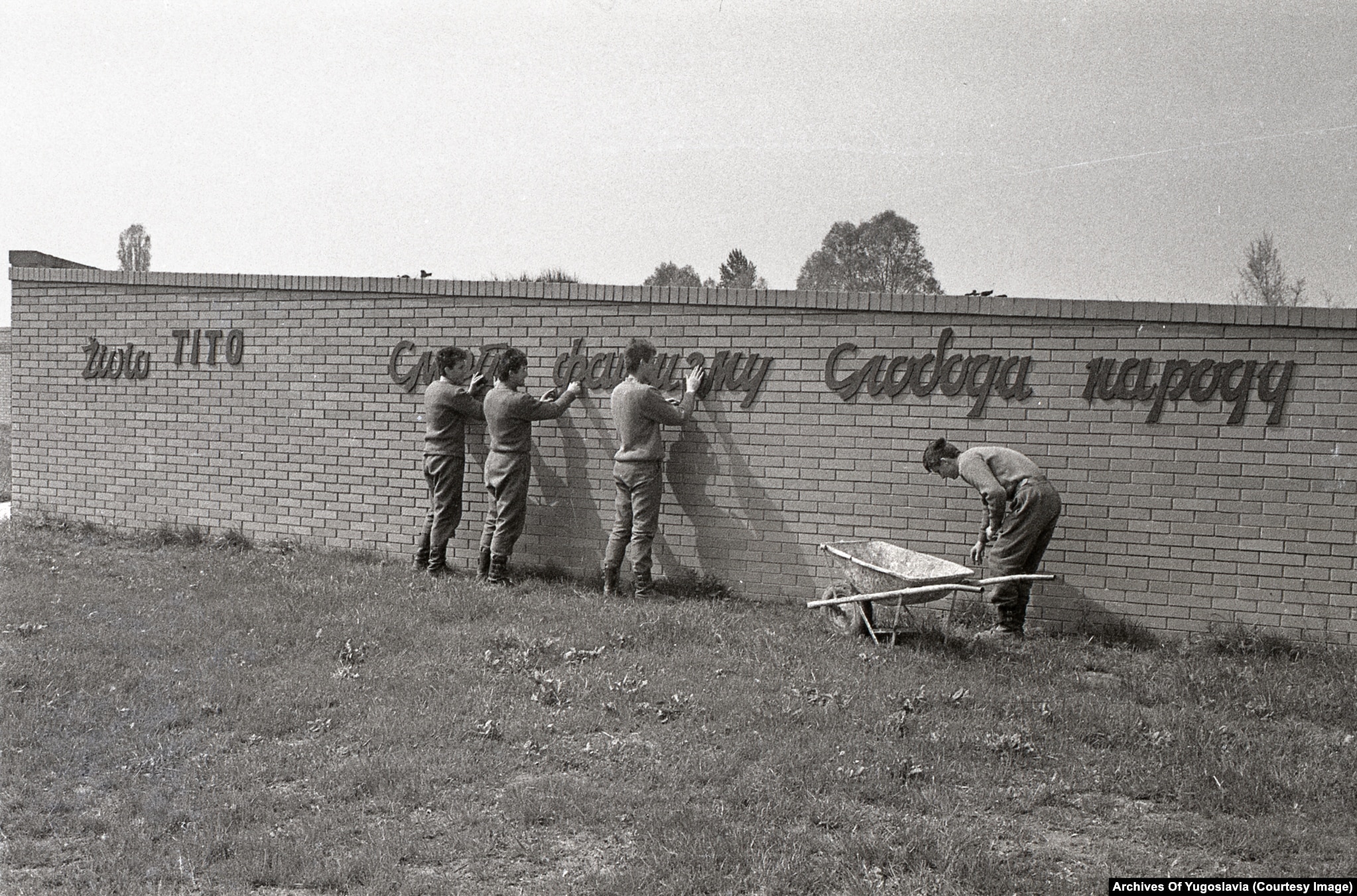 Young men in work clothes on ladders and scaffolding at the saucer-shaped Sremski Front memorial, 1988.